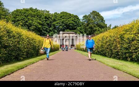 Haddington, East Lothian, Scozia, Regno Unito, 15th luglio 2020. Amisfield Walled Garden riapre: Giardino del 18th ° secolo, uno dei più grandi in Scozia. E 'ora aperto 3 giorni alla settimana con un sistema di prenotazione online dopo le restrizioni di blocco attenuati durante la pandemia di Covid-19. Kate e Claire portano un pic-nic a piedi lungo un ampio sentiero che conduce lontano dalla struttura ad angolo fiancheggiata da siepi nel sole estivo Foto Stock