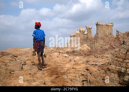 Uomo nero della tribù Afar e torri e pinnacoli composti di sale, potassio e magnesio nel deserto del Danakil, Etiopia, Africa Foto Stock