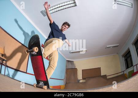 Skateboarder che esegue un trucco sulla mini rampa presso lo skate Park al coperto. Foto Stock