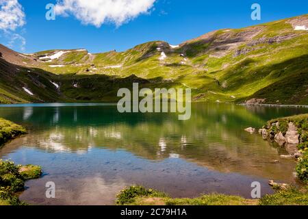 Cresta montana con piccoli punti di neve che si riflettono in un piccolo lago di montagna vicino al Bachalpsee, in alto sulle montagne bernesi. Grindelwald, Berner Foto Stock