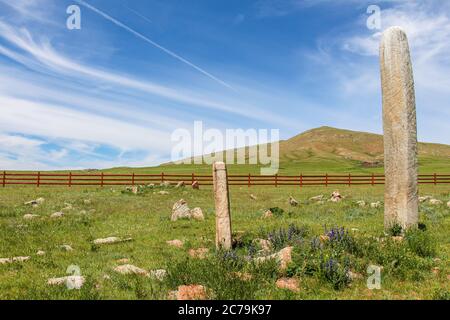 Pietre di cervo in piedi in su una collina mongolo, con una recinzione rossa nel terreno del bacck e cieli blu Foto Stock