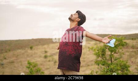 giovane uomo che sente aria fresca rimuovendo maschera medica sulla cima della montagna - concetto di gioia da ossessione maschera o è uscito dopo coronavirus o covid-19 Foto Stock