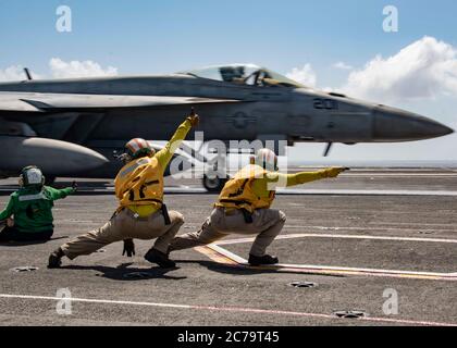 L'equipaggio della marina statunitense segnala un F/A-18E Super Hornet aereo da combattimento, attaccato a Royal Maces di Strike Fighter Squadron 27, per il lancio sul ponte di volo della portaerei di classe Nimitz USS Ronald Reagan 14 luglio 2020 in corso nel . Foto Stock