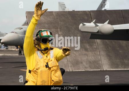 Una giacca gialla della Marina degli Stati Uniti dirige un aereo da combattimento F/A-18F Super Hornet, proveniente dai Diamondbacks dello Strike Fighter Squadron 102, per prepararsi al lancio sul ponte di volo della portaerei di classe Nimitz USS Ronald Reagan durante le operazioni del 21 giugno 2020 nel Mare delle Filippine. Foto Stock