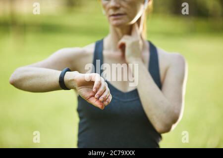 Primo piano di una donna sportiva che misura l'impulso controllando il tempo dopo l'allenamento in parcheggio Foto Stock