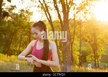 Donna che controlla il dispositivo indossabile per il monitoraggio della salute e del fitness nel parco. Foto Stock