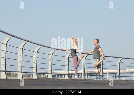 Coppia sportiva matura in piedi su ringhiera e gambe stretching mentre si allenano insieme Foto Stock