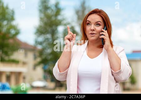 Comunicazioni. Ritratto di una bella donna caucasica più taglia, chiamando al telefono. Esterno. Concetto di business, freelance e comunicazione. Foto Stock