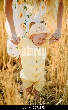 La madre conduce e tiene per mano il suo bambino piangente in campo di grano giallo. Foto Stock