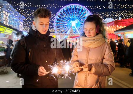 Felice coppia adolescente con sparklers che festeggia e divertirsi al mercato di Natale Foto Stock