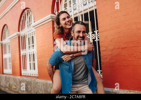 Coppia piggybacking all'aperto sulla strada della città. Uomo che porta la donna sulla schiena. Foto Stock