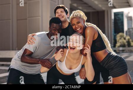 Gruppo multietnico di giovani donne si allenano all'aperto in città. Uomini e donne in abiti sportivi in piedi insieme e ridendo. Foto Stock