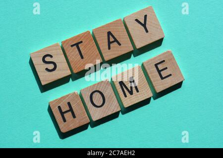 Rimani a casa, parole in lettere alfabetiche in legno isolate in verde Foto Stock
