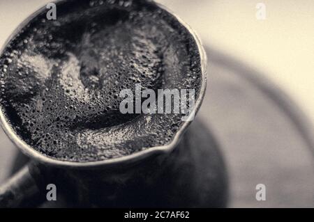 Caffè naturale con spessa schiuma, preparato in rame cezve in modo classico, su sfondo ligneo, macro foto. Foto Stock