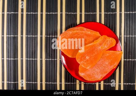 Fette di mango essiccato in un piatto rosso su un tappetino di bambù, guardaroba. Foto Stock