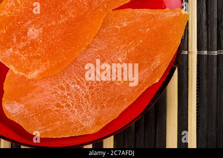 Fette di mango essiccato in un piatto rosso su un tappetino di bambù, guardaroba. Foto Stock