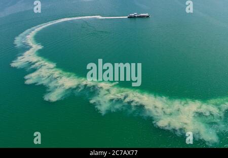 14 luglio 2020, Brandenburg, Sedlitz: Il serbatoio di trattamento delle acque Klara della Lausitzer und Mitteldeutsche Bergbau-Verwaltungsgesellschaft mbH (LMBV) sta diffondendo calce viva nelle acque del lago di Sedlitz per migliorare la qualità dell'acqua (foto aerea con un drone). La miniera a cielo aperto di Sedlitz è stata limata per conto della LMBV da giugno. Questa prima neutralizzazione viene effettuata con il proprio serbatoio di trattamento delle acque della LMBV Klara, già in funzione sul lago Partwitz. La misura dovrebbe essere effettuata entro la fine di settembre. Circa 10,000 tonnellate di cosiddetto quicklim Foto Stock