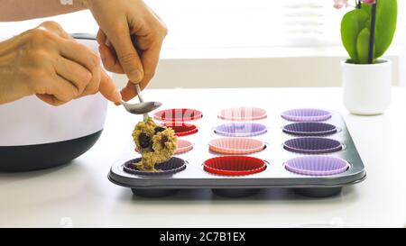 Muffin Bran con ricetta di mirtilli rossi secchi. Riempire le tazze in silicone con l'impasto per muffin da vicino su sfondo bianco Foto Stock