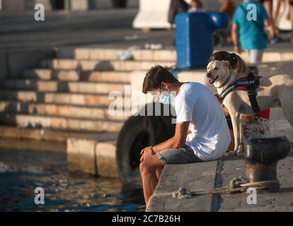 Malaga, Spagna. 15 luglio 2020. Un uomo che indossa una maschera con il suo cane siediti sul lungomare della passeggiata 'Muelle uno' durante il primo giorno di uso obbligatorio di maschere per il viso. Nuove infezioni da coronavirus in Spagna dopo l'allentamento delle restrizioni hanno indotto il governo regionale ad imporre l'uso obbligatorio di maschere facciali all'aperto e in luoghi chiusi e spiagge, anche quando osservano una distanza di sicurezza tra le persone. Questa misura cerca di frenare la diffusione della pandemia del coronavirus. Credit: SOPA Images Limited/Alamy Live News Foto Stock