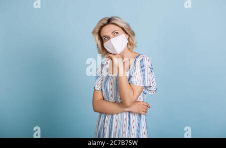 Donna caucasica premurosa con capelli biondi che toccano il mento e che si posa in un abito su una parete blu in studio Foto Stock