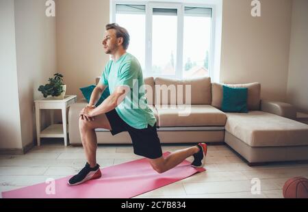 Vista laterale foto di un uomo sportivo che fa il fitness a casa su un tappeto sportivo durante la quarantena Foto Stock