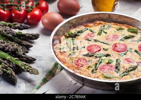 Frittata fatta di uova, asparagi e pomodori ciliegini su una padella. Cucina italiana Foto Stock