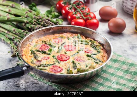 Frittata fatta di uova, asparagi e pomodori ciliegini su una padella. Cucina italiana Foto Stock