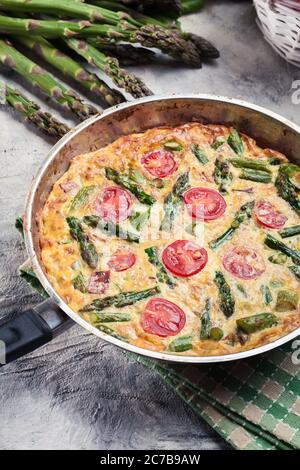 Frittata fatta di uova, asparagi e pomodori ciliegini su una padella. Cucina italiana Foto Stock