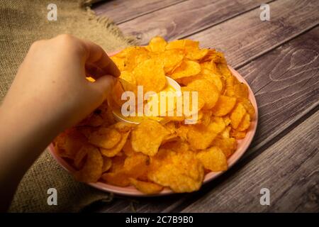 La ragazza prende un chip da un piatto rotondo con patatine e una pentola con salsa di formaggio al centro del piatto. Primo piano Foto Stock