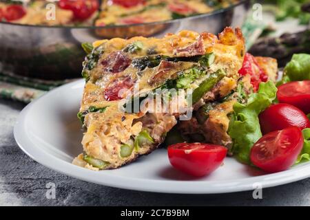 Porzione di frittata. Composto da uova, asparagi e pomodori ciliegini. Cucina italiana Foto Stock