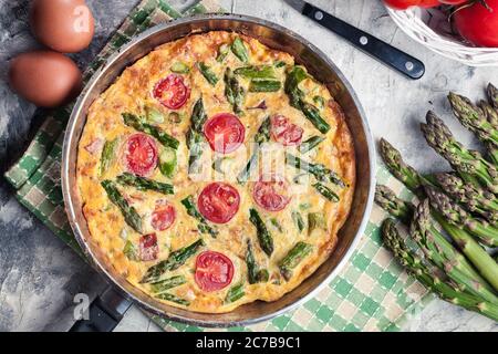 Frittata fatta di uova, asparagi e pomodori ciliegini su una padella. Cucina italiana Foto Stock