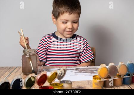 Un ragazzino di 2-3 anni in una T-shirt multicolore a righe disegna vernici guasya su carta. Tempo libero e intrattenimento per bambini, sviluppo bambini Foto Stock