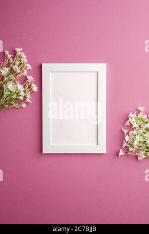 Bianco mockup cornice foto vuota con mouse-orecchio fiori di ceci su sfondo rosa viola, vista dall'alto spazio copia Foto Stock