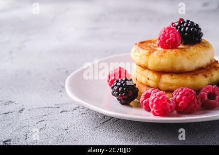 Frittelle al formaggio di cottage, frittelle di cagliata dessert con lampone e frutti di mora in piastra su fondo di pietra in cemento, macro angolo vista Foto Stock