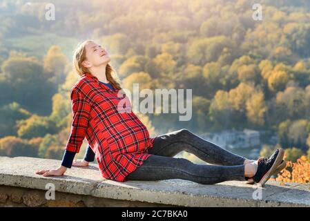 Donna incinta si trova su una collina con gli occhi chiusi. Meditazione. Autunno foresta sullo sfondo Foto Stock