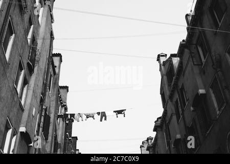 Immagine in scala di grigi ad angolo basso di abiti appesi al cavo tra alti edifici in cemento Foto Stock