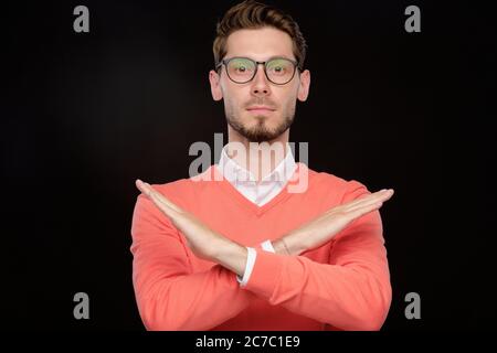 Ritratto di un uomo giovane e serio in occhiali che fa un gesto di rifiuto contro sfondo nero isolato Foto Stock