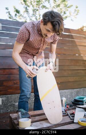 Un handyman che tiene lo skateboard e usa vernice spray Foto Stock