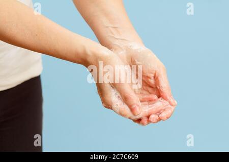 Donna lavando le mani con sapone su sfondo blu. La pulizia corretta delle mani protegge dalle infezioni. Concetto di igiene e pulizia. Foto Stock