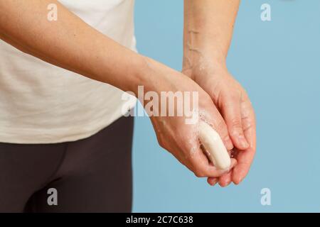 Donna che le lava le mani con sapone su sfondo blu. La corretta pulizia delle mani protegge dalle infezioni. Concetto di igiene e pulizia. Foto Stock