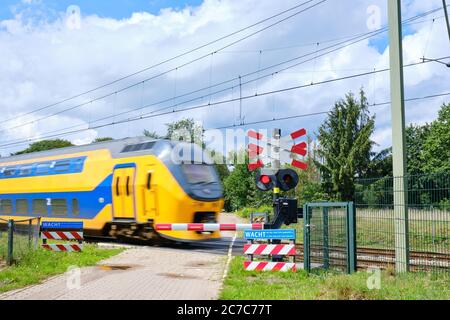 Attraversamento ferroviario con barriere e luci rosse lampeggianti e treno ad alta velocità poco affilato. Testo olandese, attendere che la luce rossa sia sparita, possibilità di altro treno Foto Stock