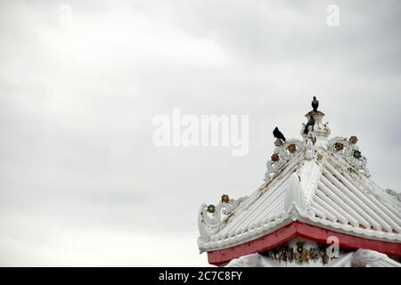 Bellissimo scatto di un tempio buddista bianco tetto con corvi seduto su di esso Foto Stock