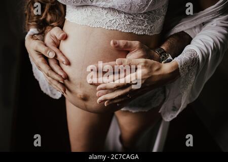 Colpo di closeup di un addome esposto di una donna incinta con un le mani dell'uomo che tengono l'addome da dietro Foto Stock