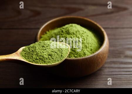 Erba di siero di latte o erba di orzo in polvere in recipiente di legno e cucchiaio su sfondo scuro. Foto Stock