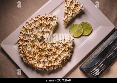 Colpo in testa di una torta di lime in un piatto, con due fette fresche di lime sul lato Foto Stock