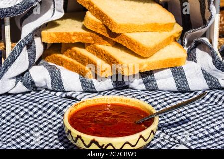 Ciotola con salsa di pomodoro e fette di pane tostato sullo sfondo in una composizione rustica. Foto Stock