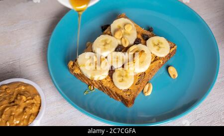 Colpo di closeup selettivo di un toast con burro di arachidi, semi vari, miele e banane Foto Stock
