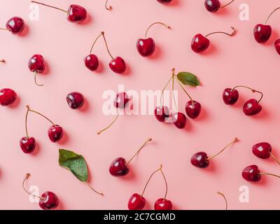 Ciliegie fresche sparse su sfondo rosa. Creativo fresco ciliegio motivo sfondo con spazio copia. Vista dall'alto o in piano. Cospargere ciliegia con foglie verdi come layout creativo per il cibo di fondo Foto Stock