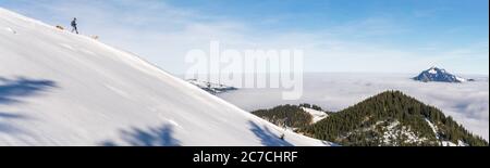 Uomo con due cani che scendono la neve montagna con vista incredibile sulle montagne sopra lo strato di nebbia valle. Mare di nuvole. Vista da Rangiswangerhorn, Alpi Foto Stock