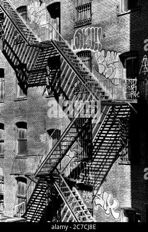 Immagine verticale in scala di grigi di scale metalliche vicino a un vecchio edificio con finestre Foto Stock